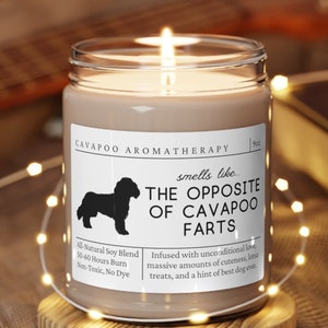 May include: A brown glass candle with a white label that reads "CAVAPOO AROMATHERAPY smells like THE OPPOSITE OF CAVAPOO FARTS". The label also includes the text "All Natural Soy Blend 50-60 Hours Burn Non-Toxic, No Dye" and "Infused with unconditional love, massive amounts of cuteness, least treats, and a hint of best dog ever."