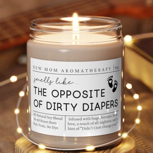 May include: A brown soy candle with a white label that reads "New Mom Aromatherapy smells like... The Opposite of Dirty Diapers". The label also includes the text "All Natural Soy Blend, 50-60 Hours Burn, Non-Toxic, No Dye" and "Infused with hugs, hiccups, love, a touch of all-nighters, and a hint of "Didn't I just change you?"