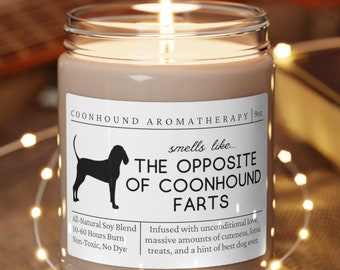 Może przedstawiać: Brązowa świeca z białą etykietą, na której widnieje napis "Coonhound Aromatherapy" i "smells like THE OPPOSITE OF COONHOUND FARTS". Etykieta zawiera również tekst "All Natural Soy Blend, 50-60 Hours Burn, Non-Toxic, No Dye" i "Infused with unconditional love, massive amounts of cuteness, treats, and a hint of best dog ever".