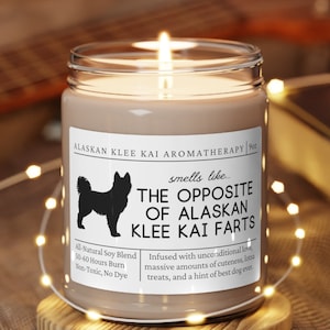 May include: A brown candle with a white label that reads "ALASKAN KLEE KAI AROMATHERAPY" and "smells like... THE OPPOSITE OF ALASKAN KLEE KAI FARTS". The label also includes the text "All Natural Soy Blend", "50-40 Hours Burn", "Non-Toxic, No Dye", "Infused with unconditional love, massive amounts of cuteness, treats, and a hint of best dog ever".