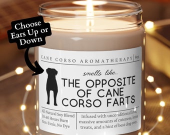 May include: A brown candle with a white label that reads "CANE CORSO AROMATHERAPY" and "smells like... THE OPPOSITE OF CANE CORSO FARTS". The label also includes the text "All-Natural Soy Blend, 50-60 Hours Burn, Non-Toxic, No Dye" and "Infused with unconditional love, massive amounts of cuteness, lots of treats, and a hint of best dog ever."