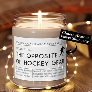 May include: A brown soy candle with a white label that reads "Hockey Coach Aromatherapy" and "Smells Like... The Opposite of Hockey Gear". The candle is on a wooden coaster and surrounded by white fairy lights.