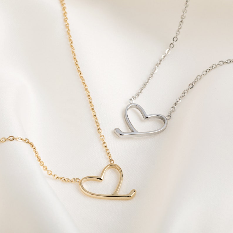 Op de afbeelding: Twee delicate kettingen met open hart hangers. De ene ketting is goud en de andere is zilver.