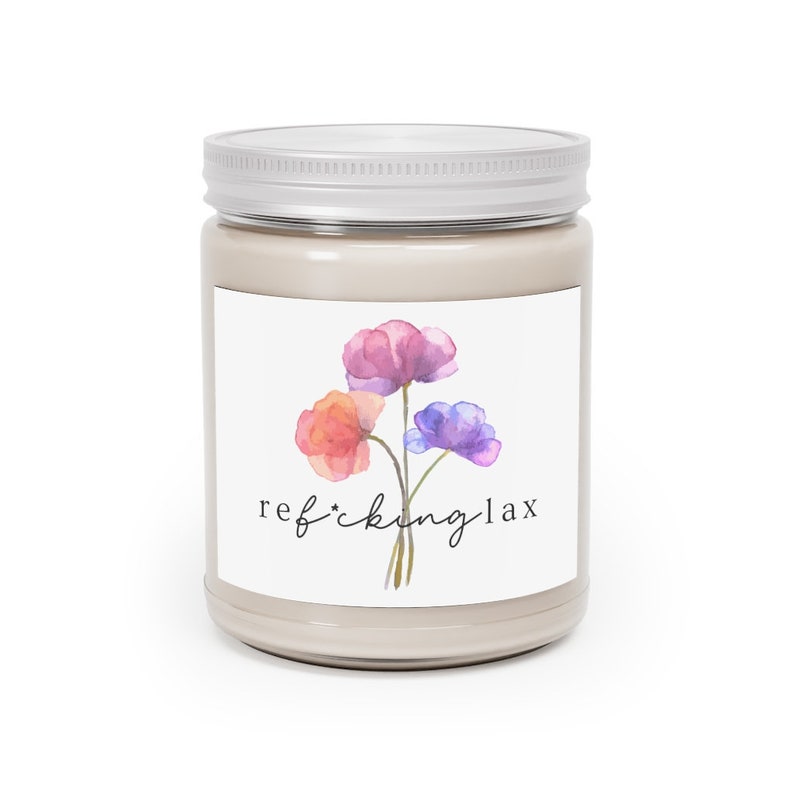 May include: A glass jar candle with a silver lid. The label features a watercolor illustration of three flowers in shades of pink, orange, and purple. The text on the label reads "ref*ckinglax".