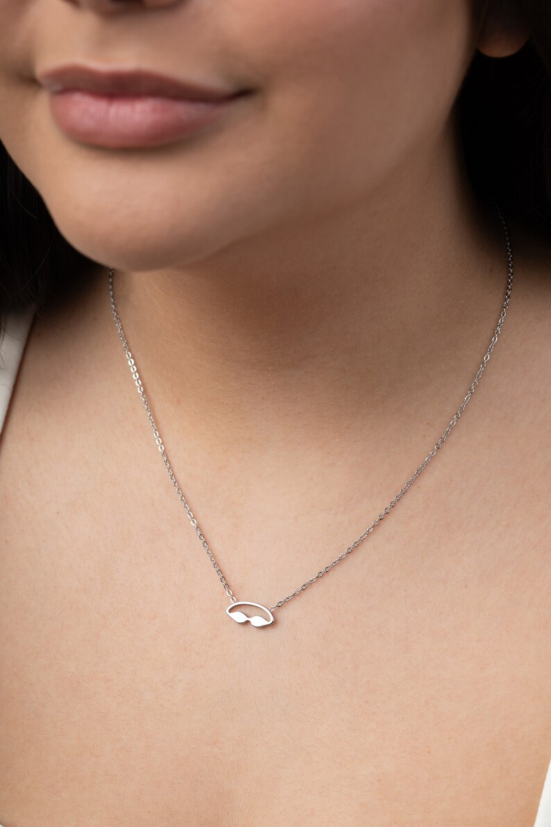 May include: A silver chain necklace with a small, silver, cutout pendant shaped like a pair of swimming goggles.