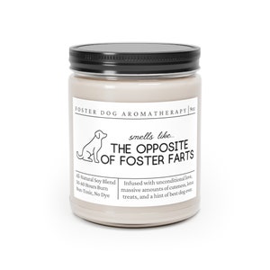 May include: A beige candle jar with a black lid and a white label that reads "FOSTER DOG AROMATHERAPY | 9oz" and "smells like... THE OPPOSITE OF FOSTER FARTS". The label also includes the text "All-Natural Soy Blend, 50-60 Hours Burn, Non-Toxic, No Dye" and "Infused with unconditional love, massive amounts of cuteness, lotsa treats, and a hint of best dog ever."