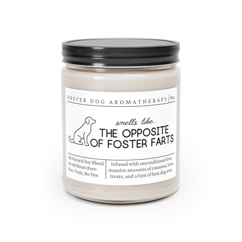 May include: A beige candle jar with a black lid and a white label that reads "FOSTER DOG AROMATHERAPY | 9oz" and "smells like... THE OPPOSITE OF FOSTER FARTS". The label also includes the text "All-Natural Soy Blend, 50-60 Hours Burn, Non-Toxic, No Dye" and "Infused with unconditional love, massive amounts of cuteness, lotsa treats, and a hint of best dog ever."