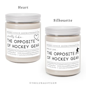 May include: Two soy wax candles with silver lids. The candles are labeled "Hockey Coach Aromatherapy" and have the text "The Opposite of Hockey Gear" on the front. One candle has a heart icon and the other has a hockey player silhouette.
