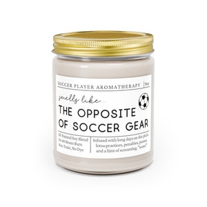 May include: A beige candle jar with a gold lid. The label reads "Soccer Player Aromatherapy" and "smells like... THE OPPOSITE OF SOCCER GEAR". The candle is infused with a scent inspired by soccer practices, penalties, passes, and a hint of screaming. The candle is made with all-natural soy blend and has a 50-60 hour burn time. It is non-toxic and dye-free.