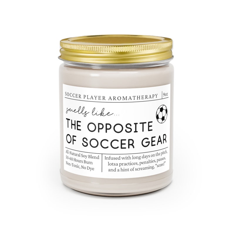 May include: A beige candle jar with a gold lid. The label reads "Soccer Player Aromatherapy" and "smells like... THE OPPOSITE OF SOCCER GEAR". The candle is infused with a scent inspired by soccer practices, penalties, passes, and a hint of screaming. The candle is made with all-natural soy blend and has a 50-60 hour burn time. It is non-toxic and dye-free.