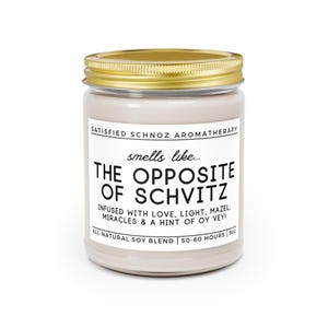 May include: A white candle jar with a gold lid. The label reads "SATISFIED SCHNOZ AROMATHERAPY" and "smells like... THE OPPOSITE OF SCHVITZ". The label also says "INFUSED WITH LOVE, LIGHT, MAZEL, MIRACLES & A HINT OF OY VEY!" and "ALL-NATURAL SOY BLEND | 50-60 HOURS | 9oz".
