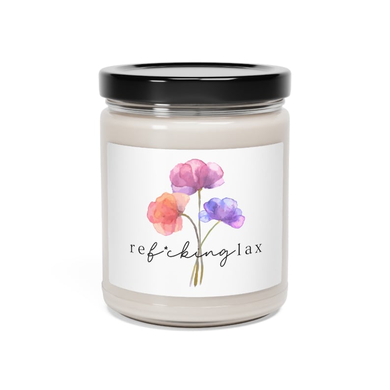 May include: A glass jar candle with a white label and a floral design. The label reads "ref*cking lax" with a watercolor illustration of three flowers in shades of pink, orange, and purple.