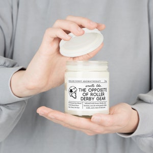 Może przedstawiać: Biały słoik ze świecą z czarną i białą etykietą, na kt&oacute;rej widnieje napis "Roller Derby Aromatherapy pachnie jak... Przeciwieństwo sprzętu do roller derby". Etykieta zawiera r&oacute;wnież małą ilustrację kasku do roller derby. Słoik ze świecą jest trzymany przez dłonie osoby.