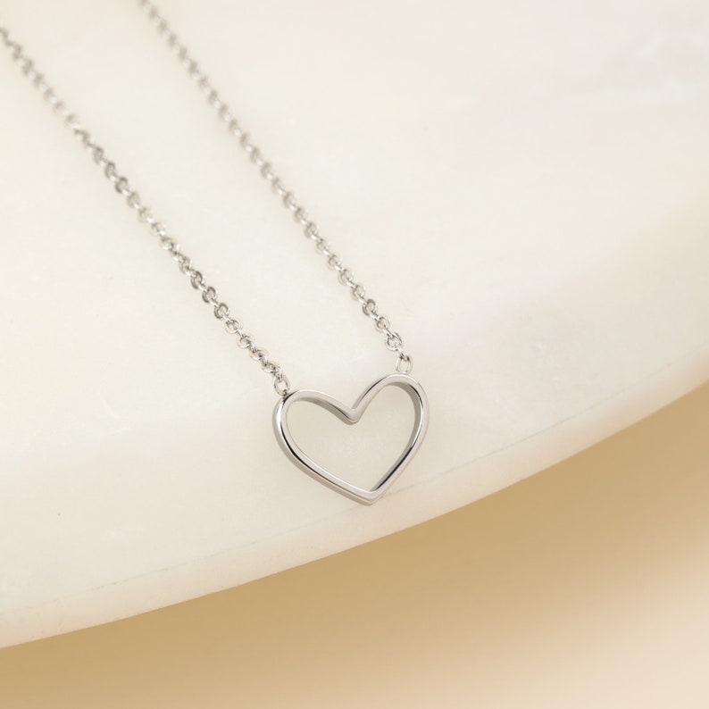 May include: A silver chain necklace with a delicate open heart pendant.