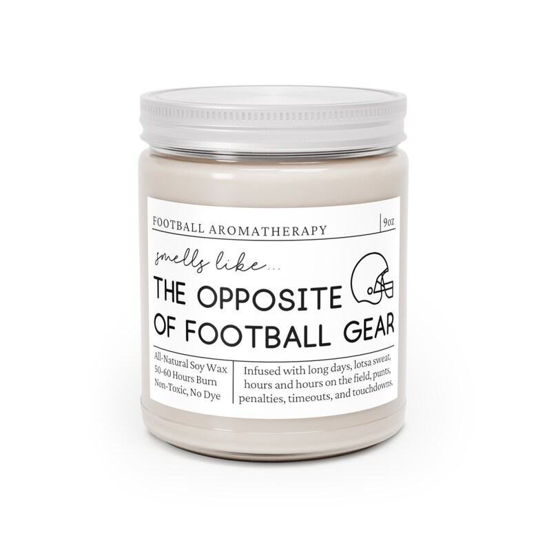 Może przedstawiać: Świeca o pojemności 9 uncji w szklanym słoiku ze srebrną pokrywką. Świeca jest beżowa i ma czarny tekst, kt&oacute;ry brzmi "Football Aromatherapy smells like... THE OPPOSITE OF FOOTBALL GEAR". Tekst kontynuuje "All-Natural Soy Wax 50-60 Hours Burn Non-Toxic, No Dye" i "Infused with long days, lotsa sweat, hours and hours on the field, punts, penalties, timeouts, and touchdowns."