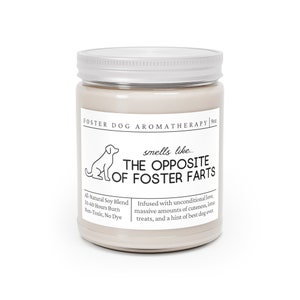 May include: A beige candle jar with a silver lid. The label reads "Foster Dog Aromatherapy" and "smells like... THE OPPOSITE OF FOSTER FARTS". The candle is made with all-natural soy blend and has a 50-60 hour burn time. It is non-toxic and dye-free.