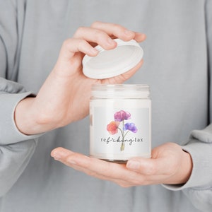 May include: A white candle jar with a floral design label. The label has a watercolor illustration of three flowers in shades of pink, purple, and orange. The text on the label reads "refikking-lax".