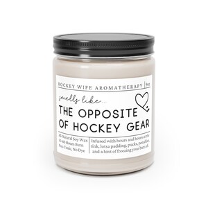 May include: A 9oz candle in a glass jar with a black lid. The label reads "Hockey Wife Aromatherapy" and "smells like... THE OPPOSITE OF HOCKEY GEAR". The candle is infused with scents of a hockey rink, padding, pucks, penalties, and a hint of freezing your butt off. The candle is made with all-natural soy wax and has a burn time of 50-60 hours.
