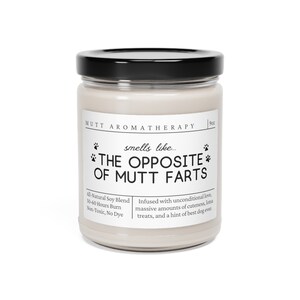 May include: A white candle jar with a black lid. The label reads "Mutt Aromatherapy" and "smells like... THE OPPOSITE OF MUTT FARTS". The candle is made with all-natural soy blend, burns for 50-60 hours, and is non-toxic and dye-free. The candle is infused with unconditional love, massive amounts of cuteness, lotsa treats, and a hint of best dog ever.