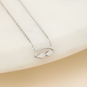 May include: A silver chain necklace with a small, silver pendant shaped like a pair of swimming goggles.