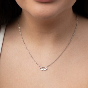 May include: A silver chain necklace with a small, minimalist pendant shaped like a pair of sunglasses.