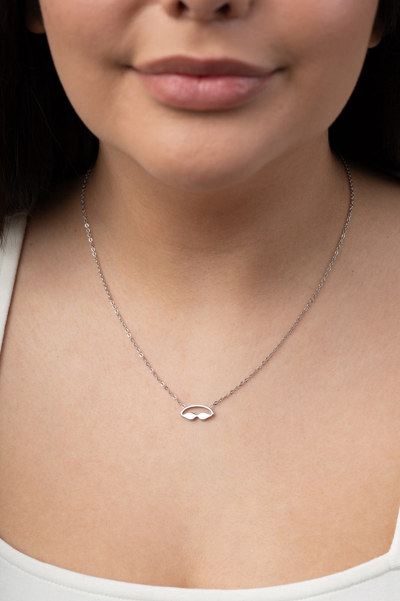 May include: A silver chain necklace with a small, minimalist pendant shaped like a pair of sunglasses.