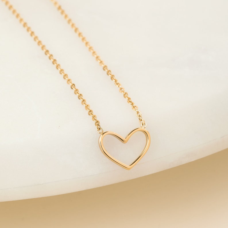 May include: A gold chain necklace with a delicate open heart pendant.