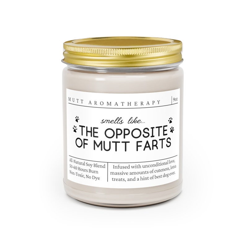 May include: A white candle jar with a gold lid. The label reads "Mutt Aromatherapy" and "smells like... THE OPPOSITE OF MUTT FARTS". The candle is infused with unconditional love, cuteness, treats, and a hint of best dog ever. It is made with a natural soy blend and burns for 50-60 hours.
