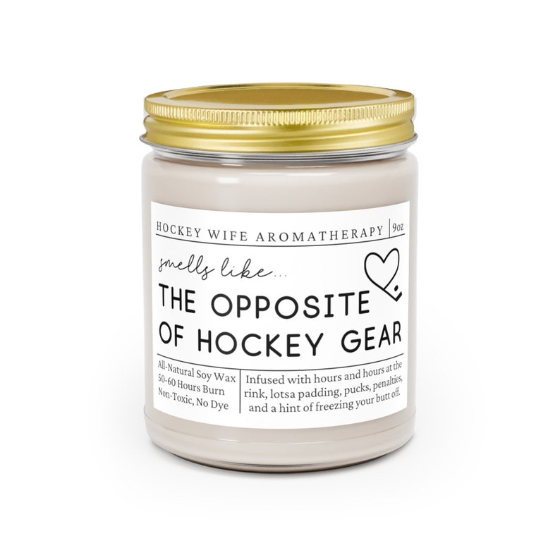 May include: A 9oz candle in a glass jar with a gold lid. The label reads "HOCKEY WIFE AROMATHERAPY" and "smells like... THE OPPOSITE OF HOCKEY GEAR". The candle is infused with scents of a hockey rink, padding, pucks, penalties, and a hint of freezing your butt off. The candle is made with all-natural soy wax and has a 50-60 hour burn time. It is non-toxic and dye-free.