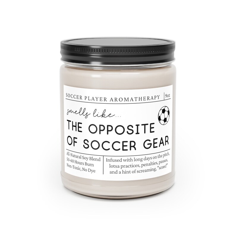 May include: A beige candle jar with a black lid and a white label that reads "Soccer Player Aromatherapy 9 oz. smells like... THE OPPOSITE OF SOCCER GEAR Al-Natural Soy Blend 50-60 Hours Burn Non-Toxic, No Dye Infused with long days on the pitch, lotsa practices, penalties, passes and a hint of screaming, "score!" "