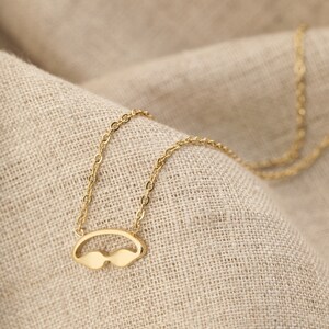 May include: A gold chain necklace with a pendant shaped like a pair of sunglasses.