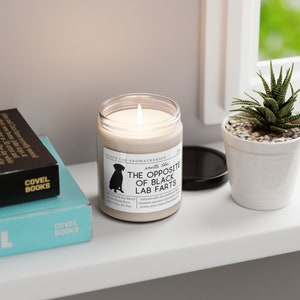 May include: A white candle with a black label that reads "Black Lab Aromatherapy" and "The Opposite of Black Lab Farts". The candle is in a glass jar with a black lid. The label also includes a silhouette of a black Labrador Retriever.