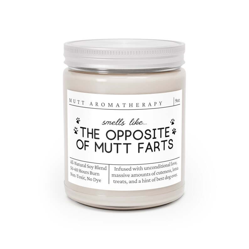 May include: A white candle jar with a silver lid. The label reads "Mutt Aromatherapy" and "smells like... THE OPPOSITE OF MUTT FARTS". The candle is made with a natural soy blend and has a burn time of 50-60 hours.