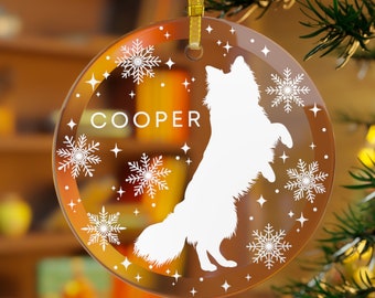 May include: A round glass Christmas ornament with a white silhouette of a dog standing on its hind legs. The ornament has a white snowflake design and the name "COOPER" printed on it.