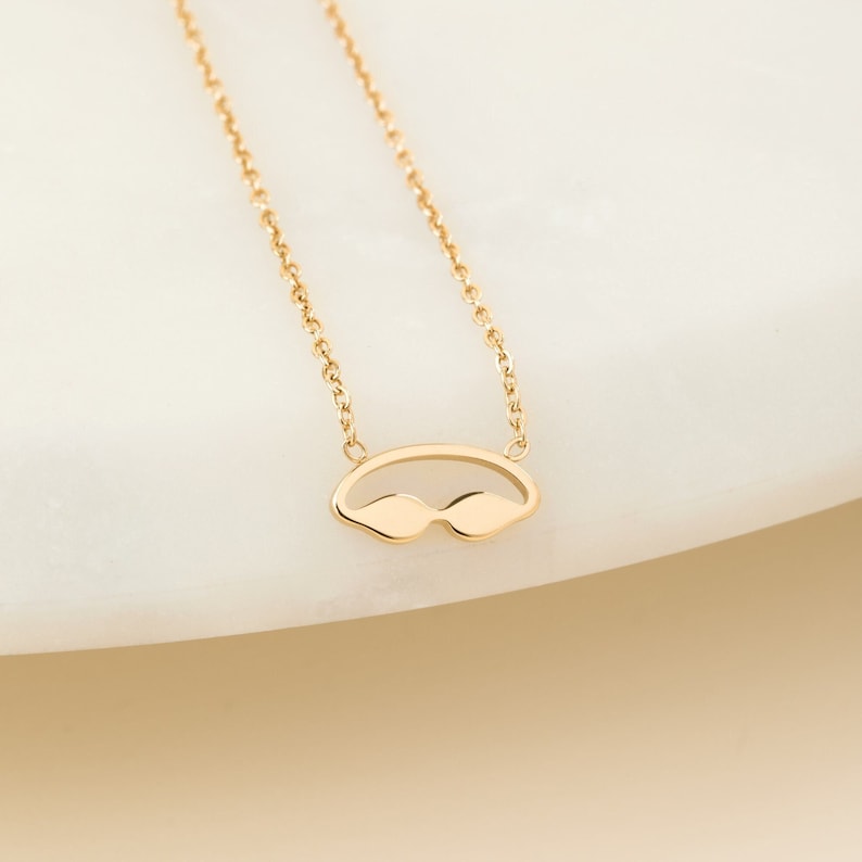May include: A gold chain necklace with a small, open-work pendant shaped like a pair of swimming goggles.