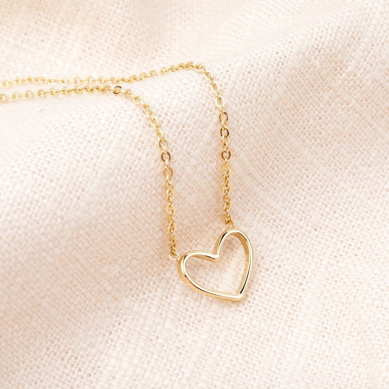 May include: A gold chain necklace with a delicate open heart pendant.