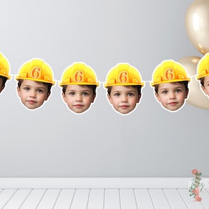 Könnte beinhalten: Eine Girlande mit sechs Ausschnitten des Gesichts eines Kindes, das einen gelben Bauhelm mit der Zahl 6 trägt. Die Girlande ist an einer weißen Schnur befestigt, mit goldenen Luftballons im Hintergrund. Geeignet für einen sechsten Geburtstag.