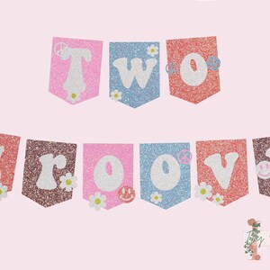 Può includere: Uno striscione scintillante con le parole "TWO GROOVY" in lettere bianche su una varietà di sfondi colorati. Lo striscione è decorato con simboli di pace e margherite.