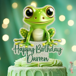 May include: Green glitter frog cake topper with the text "Happy Birthday Darren" on a green frosted cake.