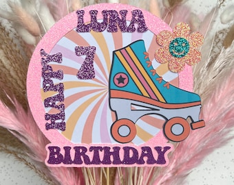 May include: A pink and purple cake topper with the words "Happy Birthday" and "Luna" in purple glitter letters. The number "7" is also in purple glitter. A roller skate with rainbow stripes and a star is on the topper. A pink flower with a smiley face is on the side.