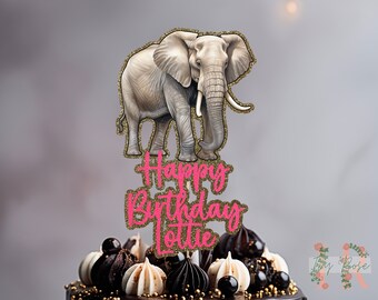 Può includere: Un topper per torta con un elefante grigio con dettagli di glitter dorati. Il topper include anche il testo "Happy Birthday Lottie" in glitter rosa.