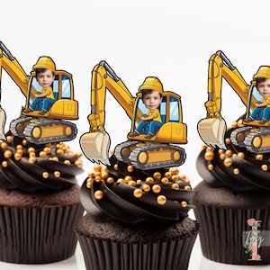 May include: Three yellow toy construction vehicle cupcake toppers with a child's face in the driver's seat. The toppers are on top of chocolate cupcakes with gold sprinkles.