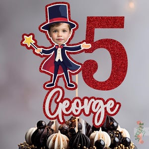 May include: Red glitter number five cake topper featuring a magician character holding a wand. The magician wears a black top hat and a red cape. The name George is written in silver glitter below the number.