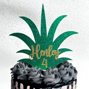 May include: Green glitter pineapple cake topper with the name "Harley" and the number "4" in gold glitter.