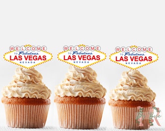 May include: Three cupcakes topped with beige frosting and decorated with a red, yellow, and blue welcome to Las Vegas sign.