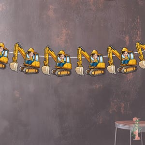 Może przedstawiać: Girlanda z żółtymi koparkami budowlanymi, każda z dzieckiem na miejscu kierowcy. Koparki mają jasnobrązową łyżkę i są połączone białą nitką. Tło jest nakrapiane brązowe.