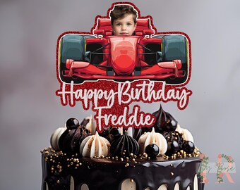 May include: A decorated cake with a red and white topper featuring a race car and the words "Happy Birthday Freddie". The cake is chocolate with white and black decorative elements.