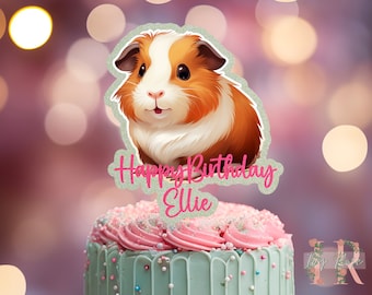 May include: A cake topper featuring a detailed illustration of a guinea pig with brown, white, and orange fur. The topper has the text "Happy Birthday Ellie" in pink glitter. The cake has a light blue base with pink frosting.