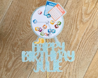 May include: A blue glitter cake topper with the words "Happy Birthday Julie" and a bingo cage with numbers.