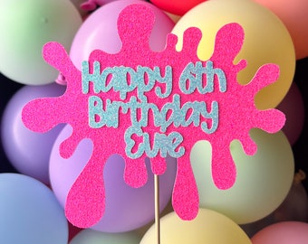 May include: Pink glitter cake topper with a pink paint splatter design. The topper says "Happy 6th Birthday Eve" in silver glitter letters.